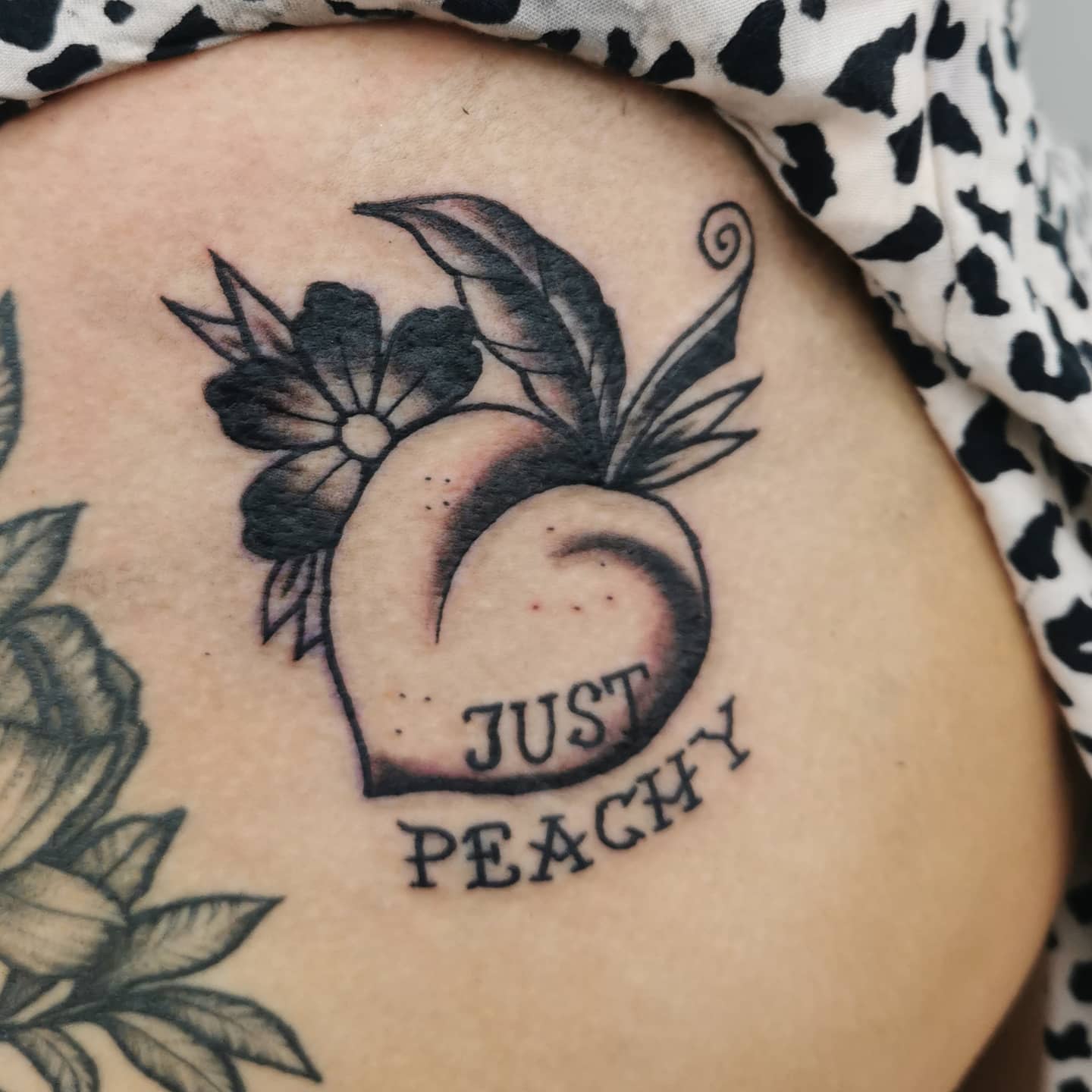 Traditional-style black and gray tattoo of a peach with leaves, a flower, and the words "Just Peachy"
